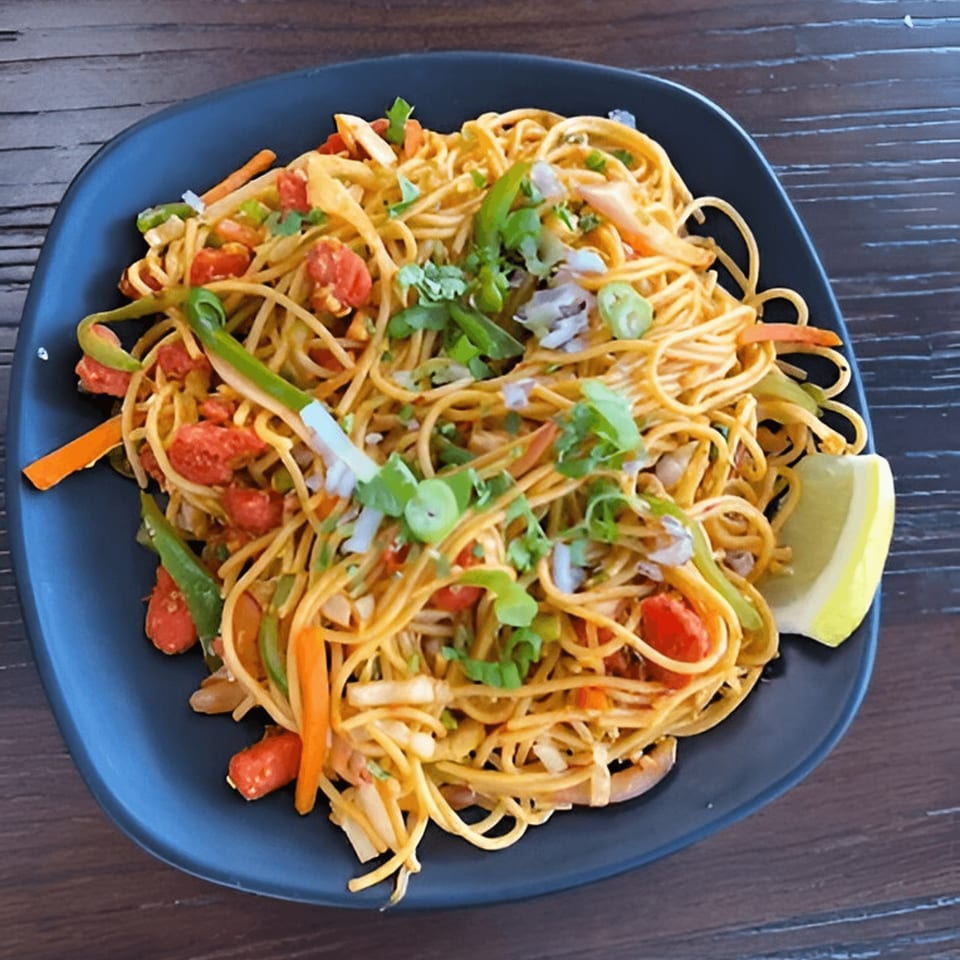 A plate of Everest Momo House's vegetable chowmein with noodles, bell peppers, tomatoes, and a lime wedge.