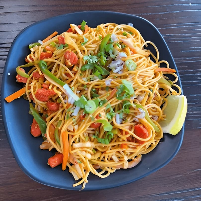 A plate of Everest Momo House's vegetable chowmein with noodles, bell peppers, tomatoes, and a lime wedge.