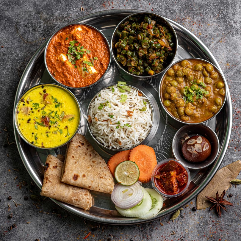 A full Everest Momo House thali with various curries, rice, flatbread, and dessert on a metal tray.
